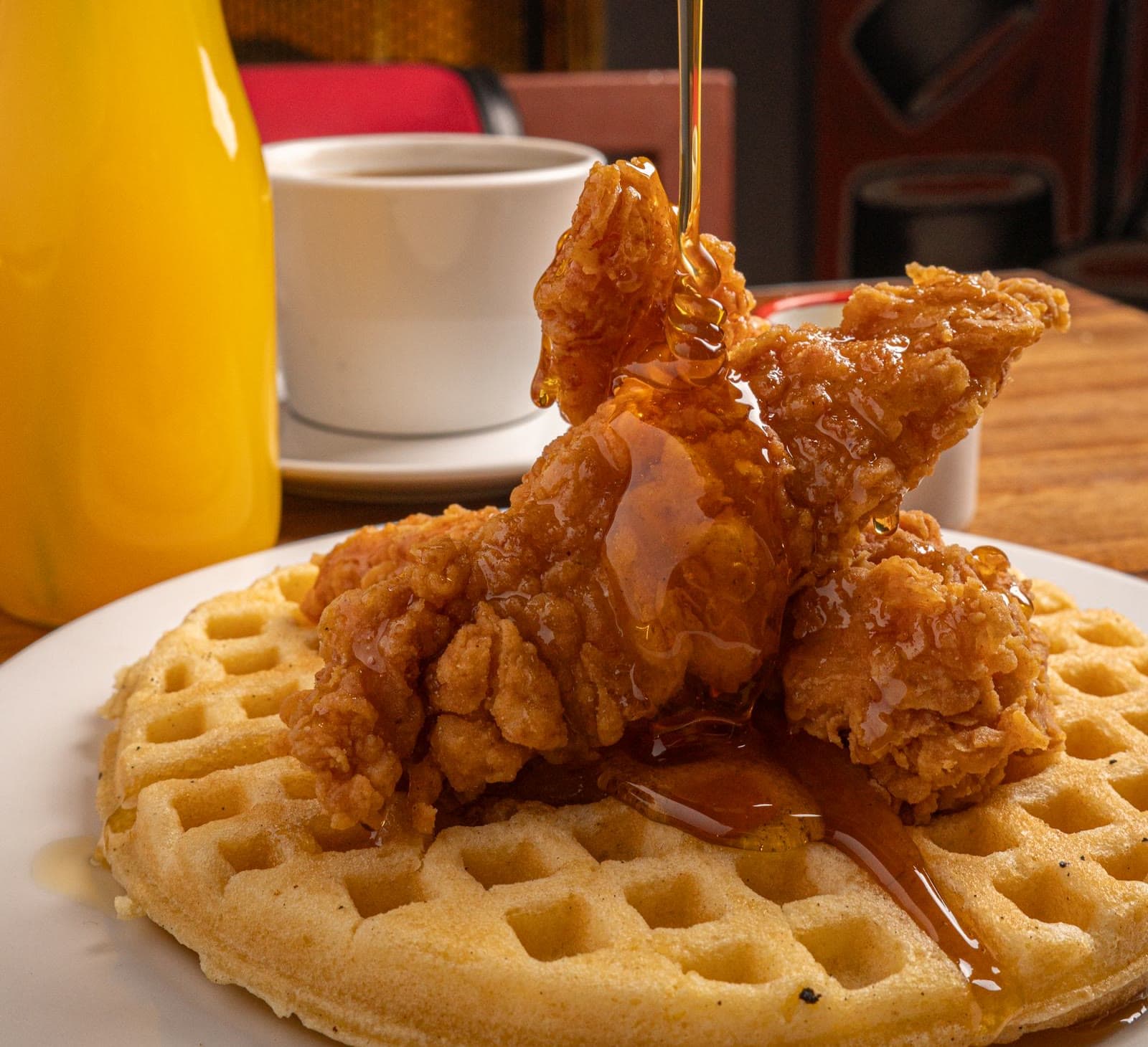 Syrup pouring over fried chicken and a waffle