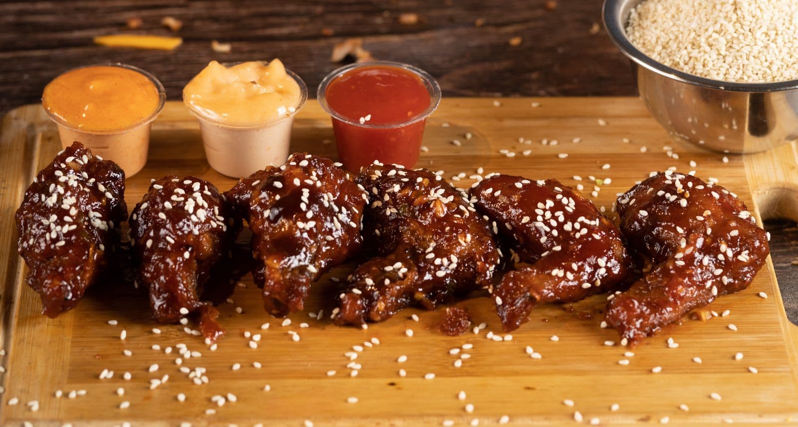 Sticky glazed wings on a board with three sauce cups